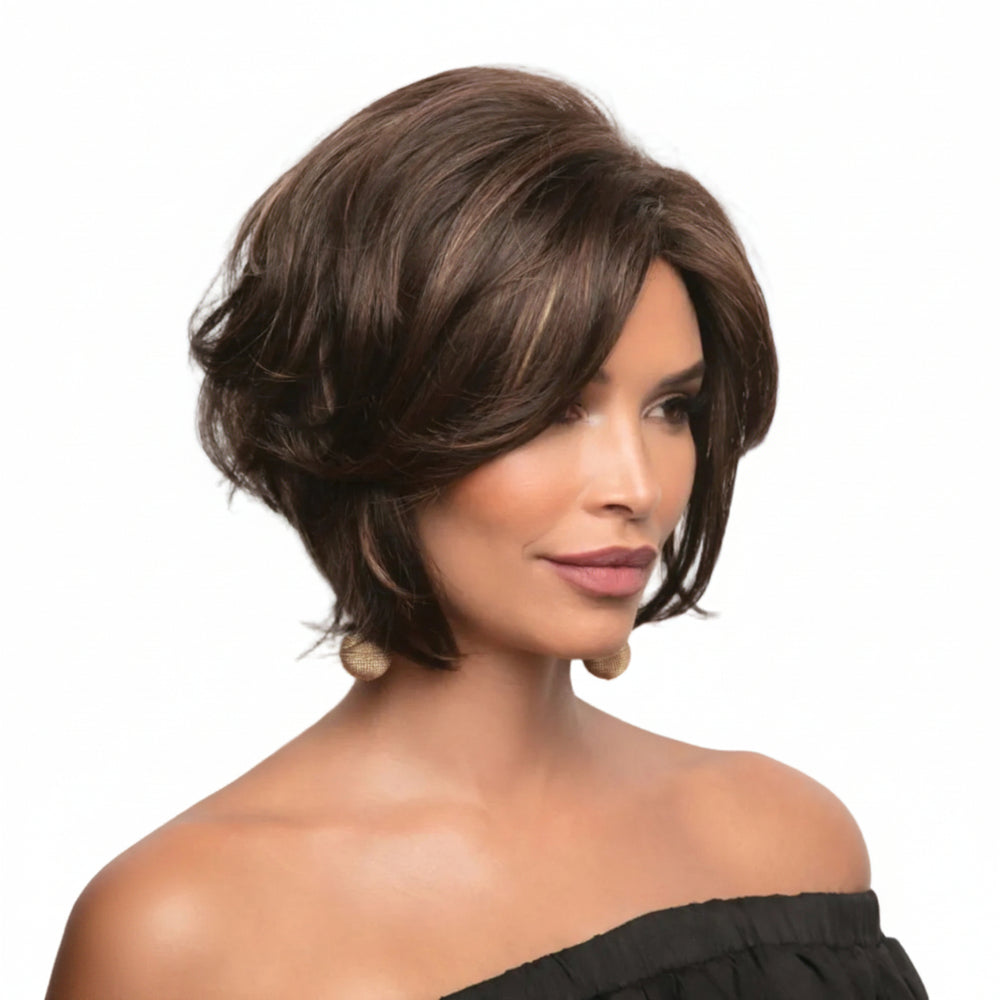 A woman modeling a short, layered brown wig with subtle lighter brown highlights, shown against a plain white background. The wig is styled with soft waves and side-swept bangs.